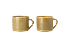 The nkuku Kalini Mugs - Green - Small (Set of 2) feature rounded bodies, large handles, and a glossy, slightly speckled finish. Shown side by side against a white background, these handmade mugs are beautifully crafted.