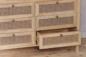 The Kanz Mango Wood Chest Of Drawers by nkuku features cane-paneled drawers with small round brass knobs, crafted from light mango wood—perfect bedroom storage. One drawer is shown partially open to reveal its spacious interior.