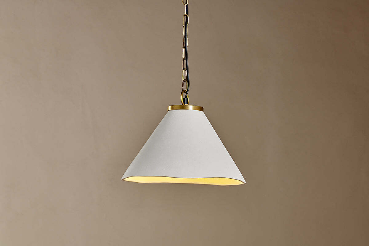 The Kiara Organic Shape Ceramic Pendant Light by nkuku features an off-white, wide cone shade and antique brass details. Hanging from a metal chain, it casts a soft downward glow—ideal for minimalist, modern kitchen lighting.