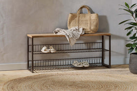 The nkuku Kiyoma Iron & Wood Low Standing Shelves in Natural display a straw tote, folded linen, and sandals. A round jute rug on the wooden floor brings warmth to the industrial space.