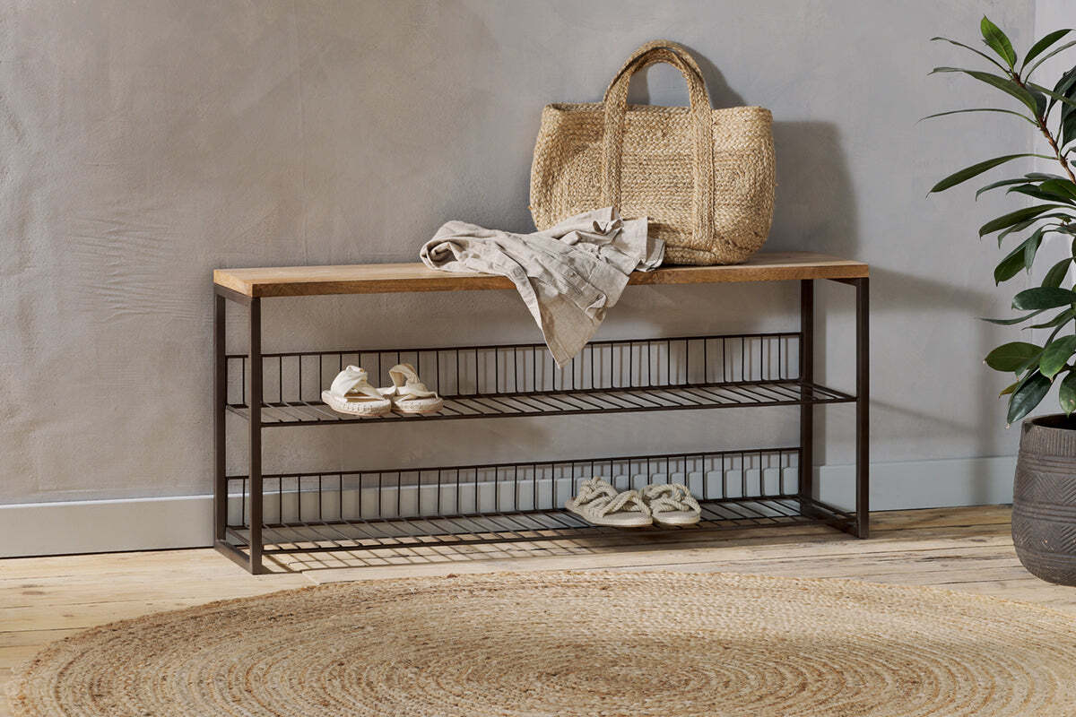 The nkuku Kiyoma Iron & Wood Low Standing Shelves in Natural display a straw tote, folded linen, and sandals. A round jute rug on the wooden floor brings warmth to the industrial space.