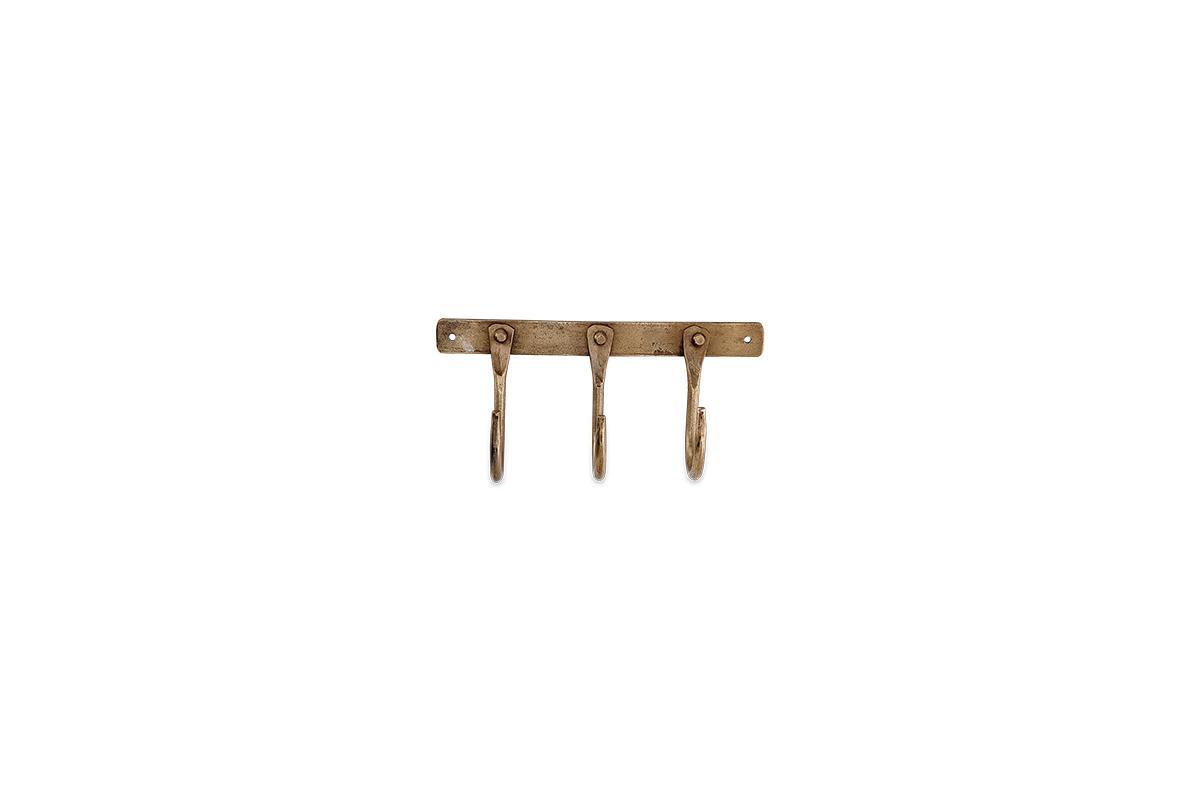 The nkuku Kuna Iron Hooks - Antique Brass features three vintage, curved iron hooks on a rectangular wall-mounted base with two visible screw holes, ideal for adding stylish, small storage to any space.