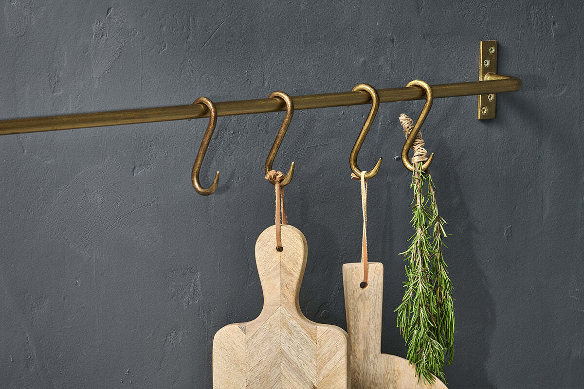 The nkuku Laila Iron S-Hooks in brass (set of 4) hold two light wood cutting boards with leather loops and a bundle of rosemary, all displayed against a matte dark gray textured wall.