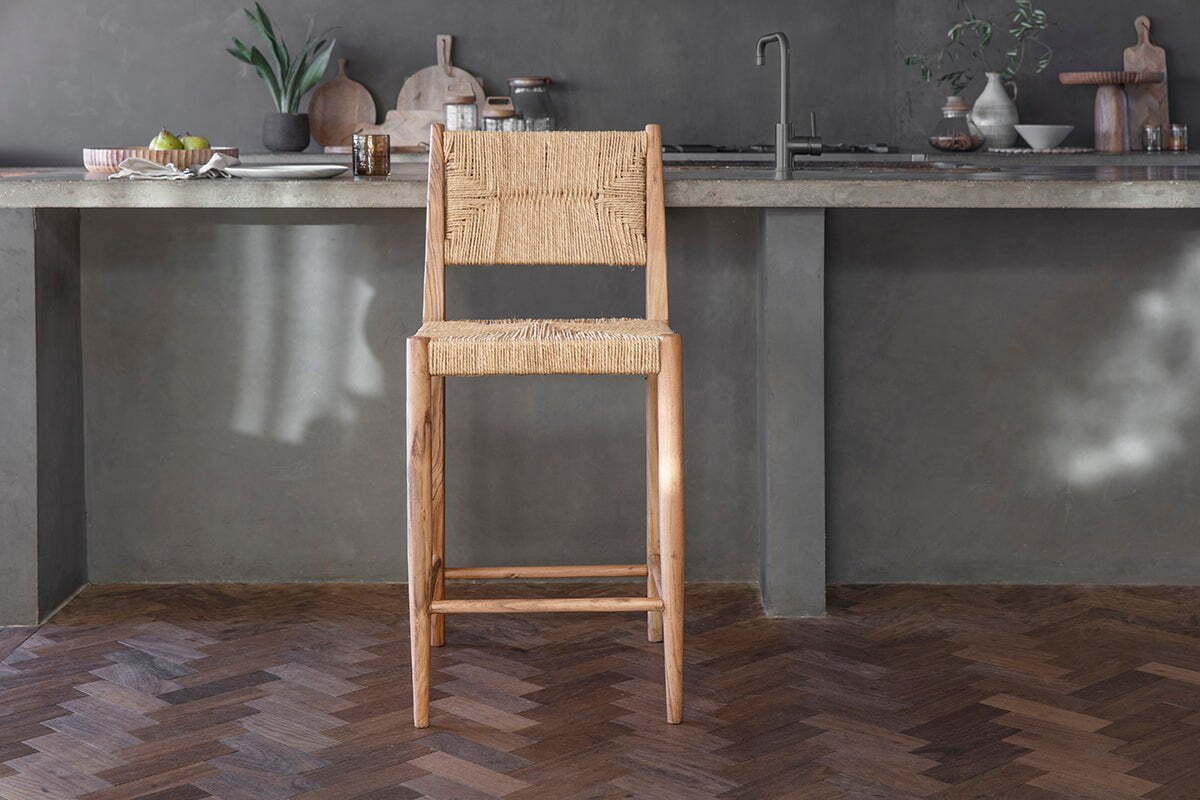 The Lohanda Acacia & Munja Grass Counter Chair by nkuku features a handcrafted light acacia wood frame with a square seat and back elegantly woven from natural munja grass, perfect for pairing with a concrete kitchen island.