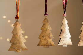 The nkuku Mishti Tree Baubles - Antique Brass - Large (Set of 4) are iron Christmas tree ornaments with a rustic, handcrafted look, hanging from ribbons against a neutral, softly lit background for a festive touch.
