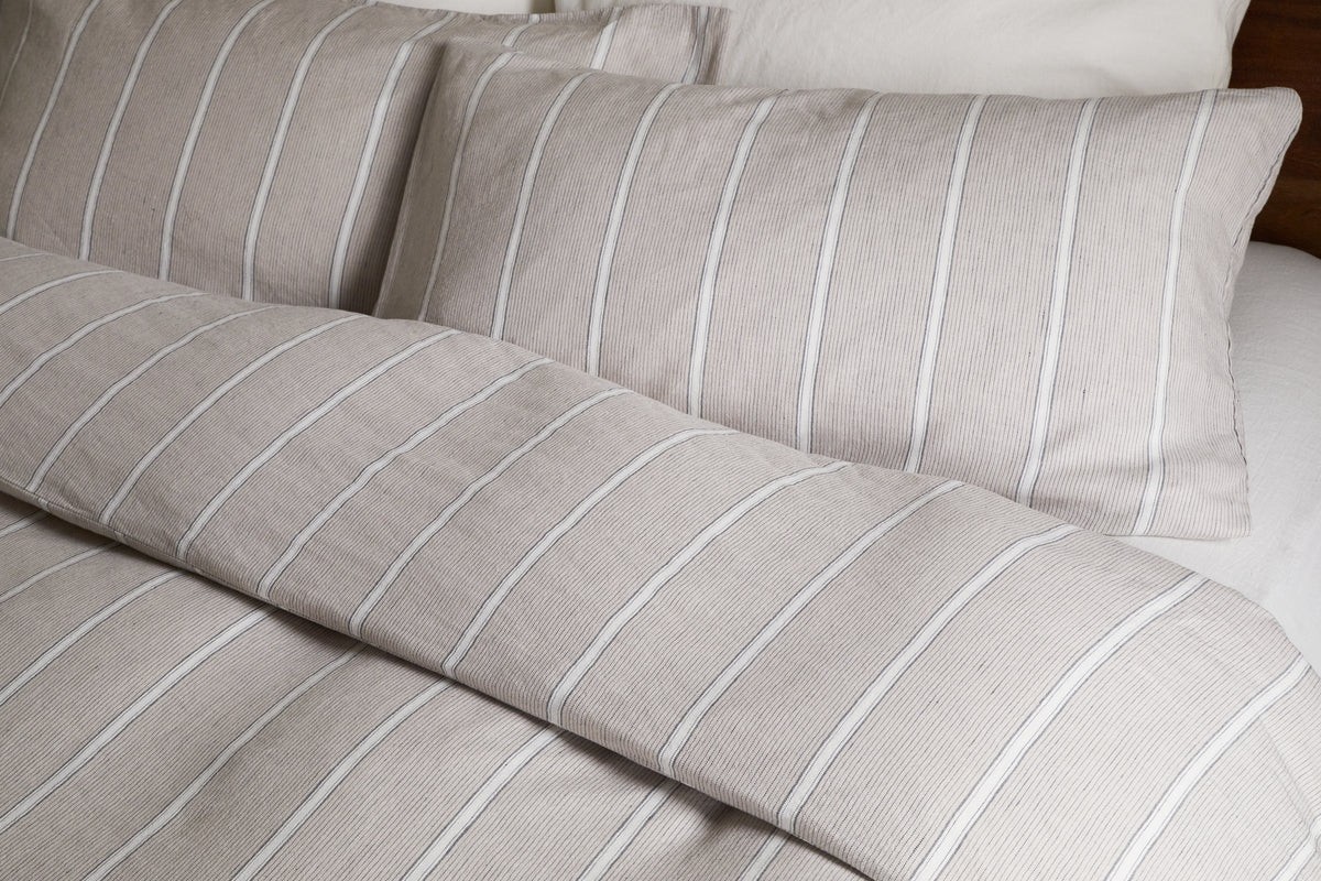 Close-up of a neatly made bed featuring the nkuku Mora Hemp & Cotton Duvet Cover in Stone Grey, paired with two matching pillowcases and crisp white sheets for breathable comfort.