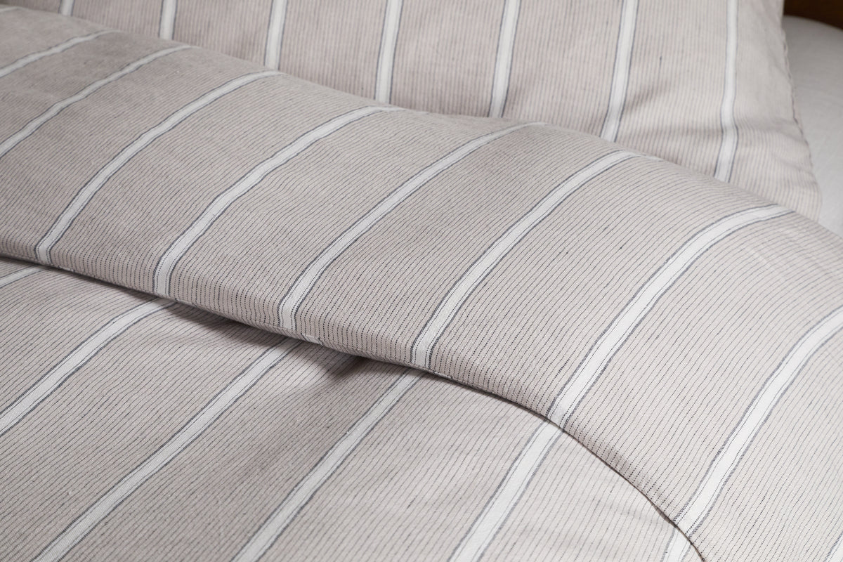 Close-up of a neatly made bed dressed in the Mora Hemp & Cotton Duvet Cover in Stone Grey by nkuku, showcasing soft, textured fabric for breathable comfort.