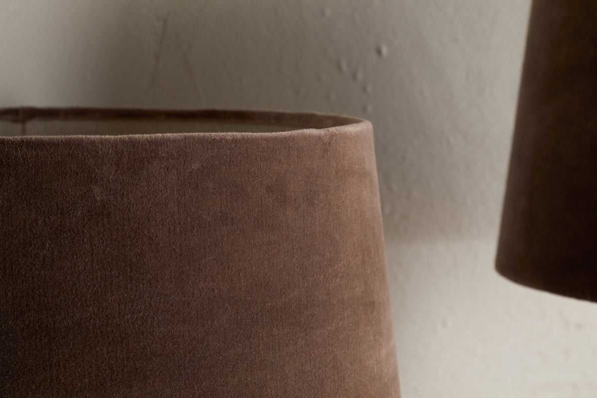 Close-up of the Mendai Velvet & Linen Lampshade in Mocha by nkuku, showing its soft brown velvet texture against a light, textured wall. The partial view highlights the smooth surface and neutral style.