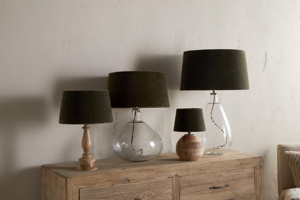 Four nkuku Mendai Velvet & Linen Lampshade lamps in moss green, with clear glass, ribbed round wood, and turned wood bases, are arranged on a wooden cabinet—creating stylish decorative lighting for any room.