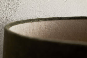 Close-up of the rim of the Mendai Velvet & Linen Lampshade in Moss Green by nkuku, showing its soft velvet curve, inner linen lining, and elegant decorative lighting details against a textured light-colored wall.