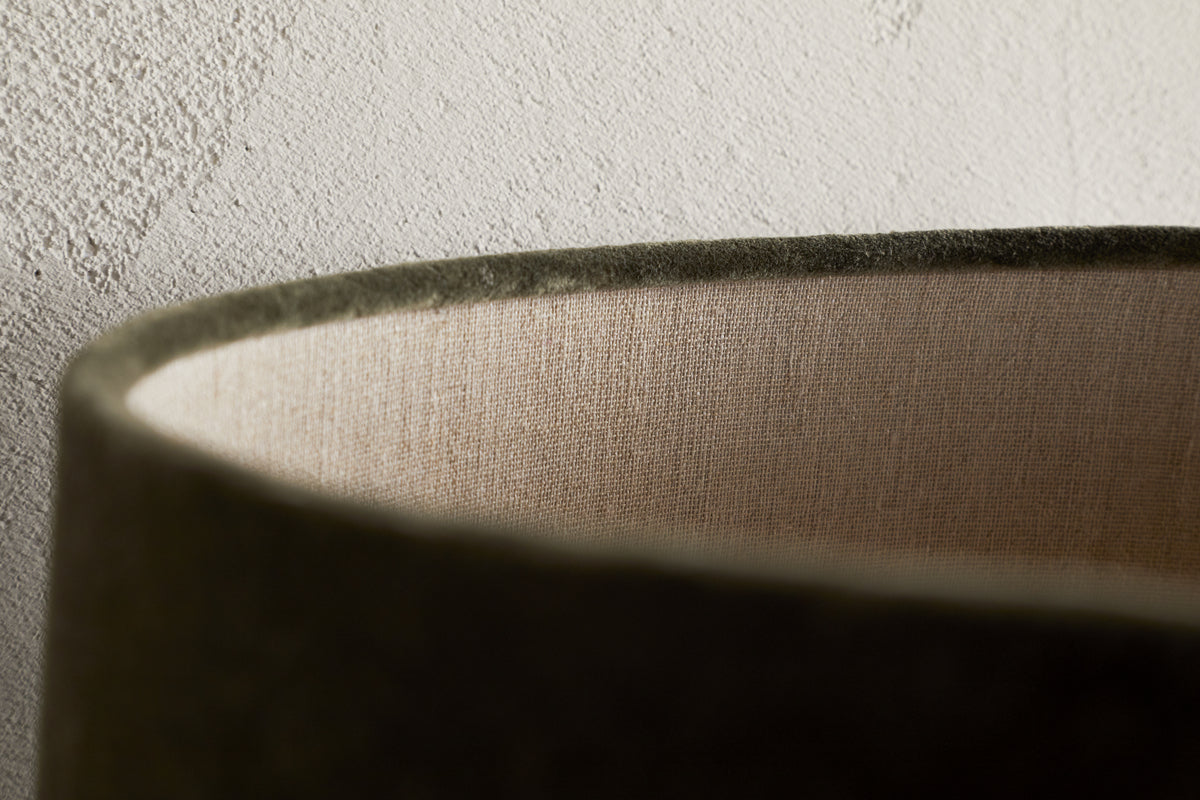 Close-up of the rim of the Mendai Velvet & Linen Lampshade in Moss Green by nkuku, showing its soft velvet curve, inner linen lining, and elegant decorative lighting details against a textured light-colored wall.