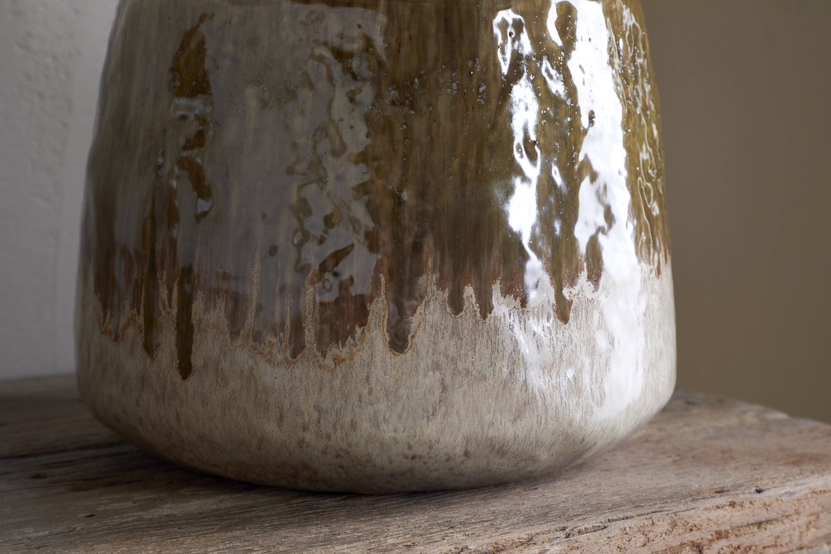 Close-up of the lower portion of the nkuku Melina Reactive Glaze Vase in Olive & Natural, showcasing its glossy finish and textured reflections as it rests on a wooden surface.