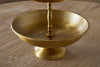 A close-up of the Mahika Stand - Antique Brass by nkuku, featuring an engraved tiered design, makes an ideal centerpiece for festive tablescapes. Shown on a wooden surface with only the lower and partial middle tier visible.