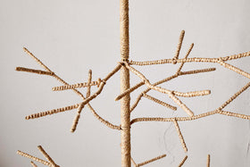 Close-up of the nkuku Mala Base Jute Tree - Natural, featuring woven jute branches and thin twine. Its sparse, angular design brings a minimalist, modern touch to festive decor against a plain light-colored wall.