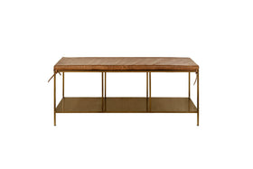 The nkuku Mahi Iron & Leather Bench features a rectangular tan leather cushion with side ties, slender brass legs, and a metal lower shelf. This minimalist bench is photographed against a plain white background.