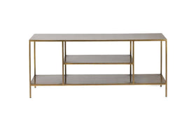 The Mahi Media Standing Shelf by nkuku features a slim gold metal frame and three rectangular wooden shelves, including two open brass shelves in the center, ideal for organizing entertainment equipment. Photographed against a plain white background.
