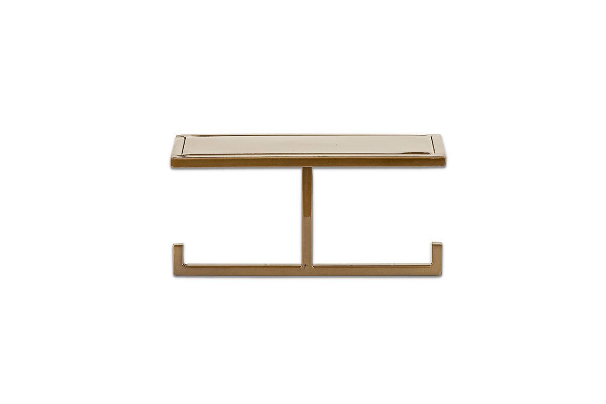 The nkuku Mahi Wall Mounted Toilet Roll Holder has a sleek, minimalist brass design with a slim top and central support on two horizontal feet, shown against a plain white background.