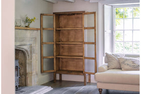 The Mendani Mango Wood & Fluted Glass Cabinet in walnut stain by nkuku sits open in a room beside a stone fireplace and a sofa.
