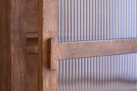Close-up of the Mendani Mango Wood & Fluted Glass Low Cabinet by nkuku, featuring a walnut-stained finish, vertical handle, and fluted glass panel in a wooden frame that highlights the wood grain, joinery, and detailed craftsmanship.