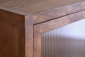 Close-up of the Mendani Mango Wood & Fluted Glass Low Cabinet by nkuku, showing vertical fluted glass on the door, reflecting light and contrasting with the warm walnut-stained finish for a modern, minimalist look.