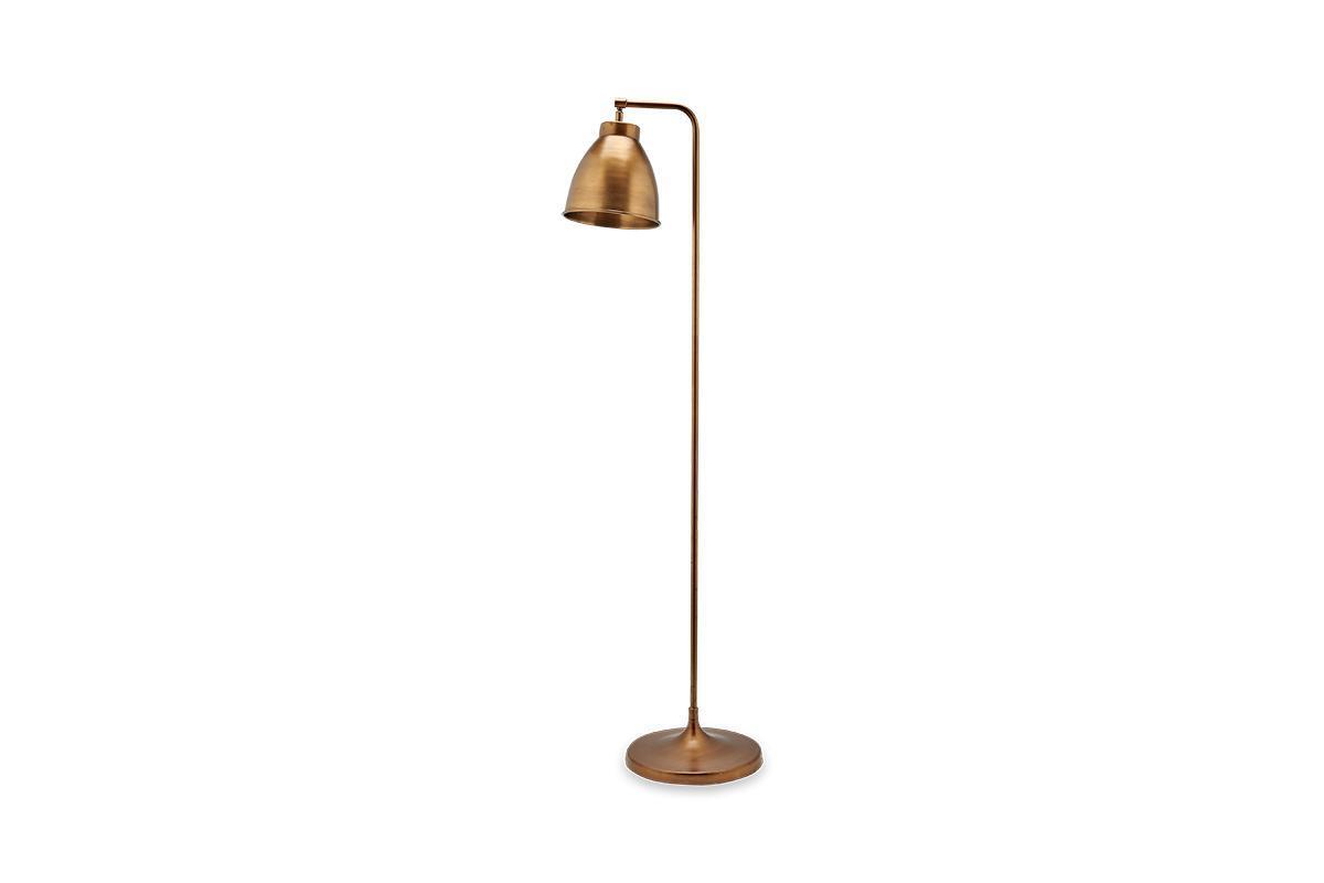 The nkuku Muturi Floor Lamp - Antique Brass features a tall, slender solid brass frame with an angled stem and round base. Its conical shade offers stylish down lighting, bringing modern elegance to any space.