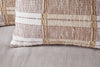 A close-up of the Nayika Cotton Cushion Cover by nkuku, featuring a woven striped pattern in rust and beige tones, resting on a light beige fabric surface.