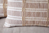 Close-up of the Nayika Cotton Cushion Cover by nkuku, featuring a cosy, textured woven pattern in rust and white stripes, displayed on a light-colored fabric surface.