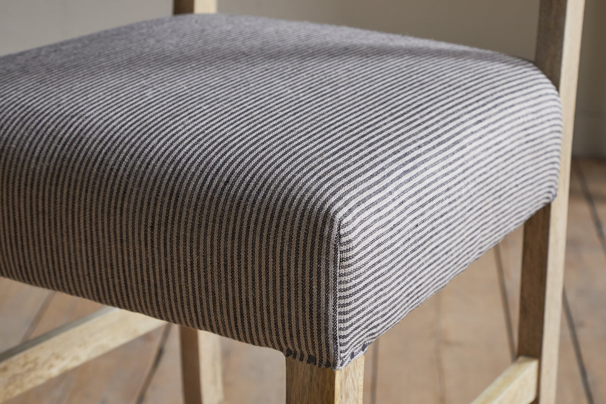 The Nadeeka Linen Upholstered Counter Chair by nkuku features a soft grey striped seat and light wood legs, making it a stylish addition to your kitchen island.