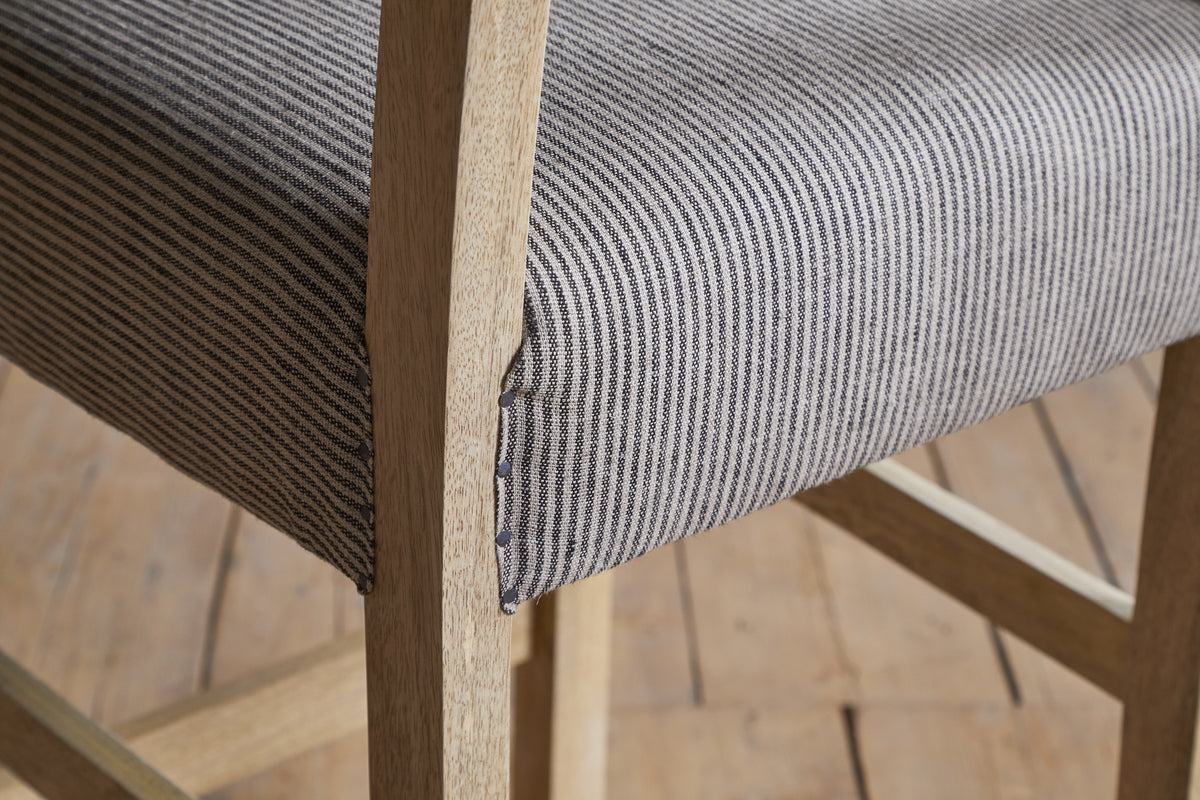 Close-up of the nkuku Nadeeka Linen Upholstered Counter Chair in soft grey, featuring a gray and white striped linen seat, shown on a light wooden floor.
