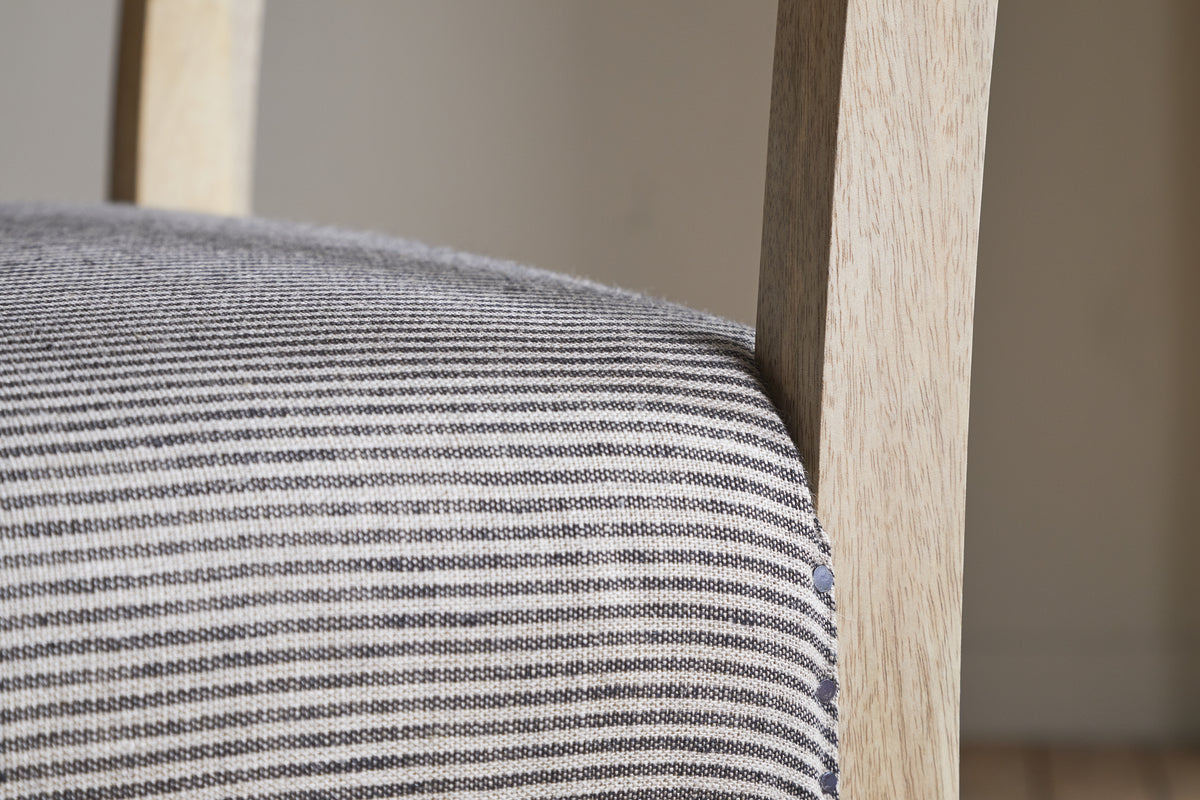 Close-up of the nkuku Nadeeka Linen Upholstered Counter Chair in soft grey, featuring textured striped linen and a light wood frame—ideal for your kitchen island.