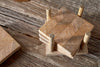 A set of four Nalbari Coasters - Natural by nkuku, featuring a chevron pattern, is stacked in a matching holder on a rustic table, with one coaster placed beside the stack.
