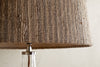 Close-up of the nkuku Nadee Banana Leaf Lampshade in Natural, featuring its textured, woven surface made from sustainable banana leaf fibers. Below, part of a clear glass base with a metallic fitting is visible.