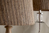 Close-up of the nkuku Nadee Banana Leaf Lampshade in natural, woven with warm brown tones, with another similar lampshade softly blurred in the background.