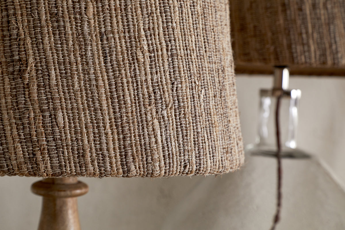 Close-up of the nkuku Nadee Banana Leaf Lampshade in natural, woven with warm brown tones, with another similar lampshade softly blurred in the background.