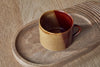 A set of two Naav Mugs - Mustard - Large by nkuku sits on a carved wooden tray with rounded grooves, displayed on a wooden surface.