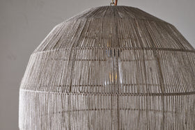 Close-up of the Nilaveli Woven Jute Sphere Pendant by nkuku, featuring a textured natural jute dome lampshade. Soft light glows through the woven strands, set against a plain, neutral background.