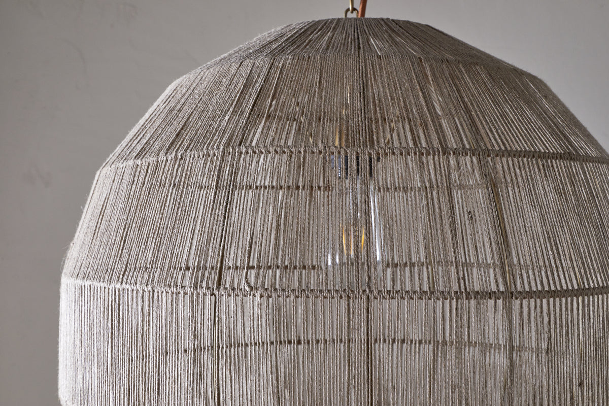 Close-up of the Nilaveli Woven Jute Sphere Pendant by nkuku, featuring a textured natural jute dome lampshade. Soft light glows through the woven strands, set against a plain, neutral background.