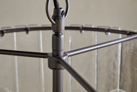 Close-up of the Nauka Statement Pendant by nkuku, featuring an aged bronze finish. The central rod links to three horizontal arms supporting a circular frame with clear glass panels, creating a refined, modern chandelier effect.
