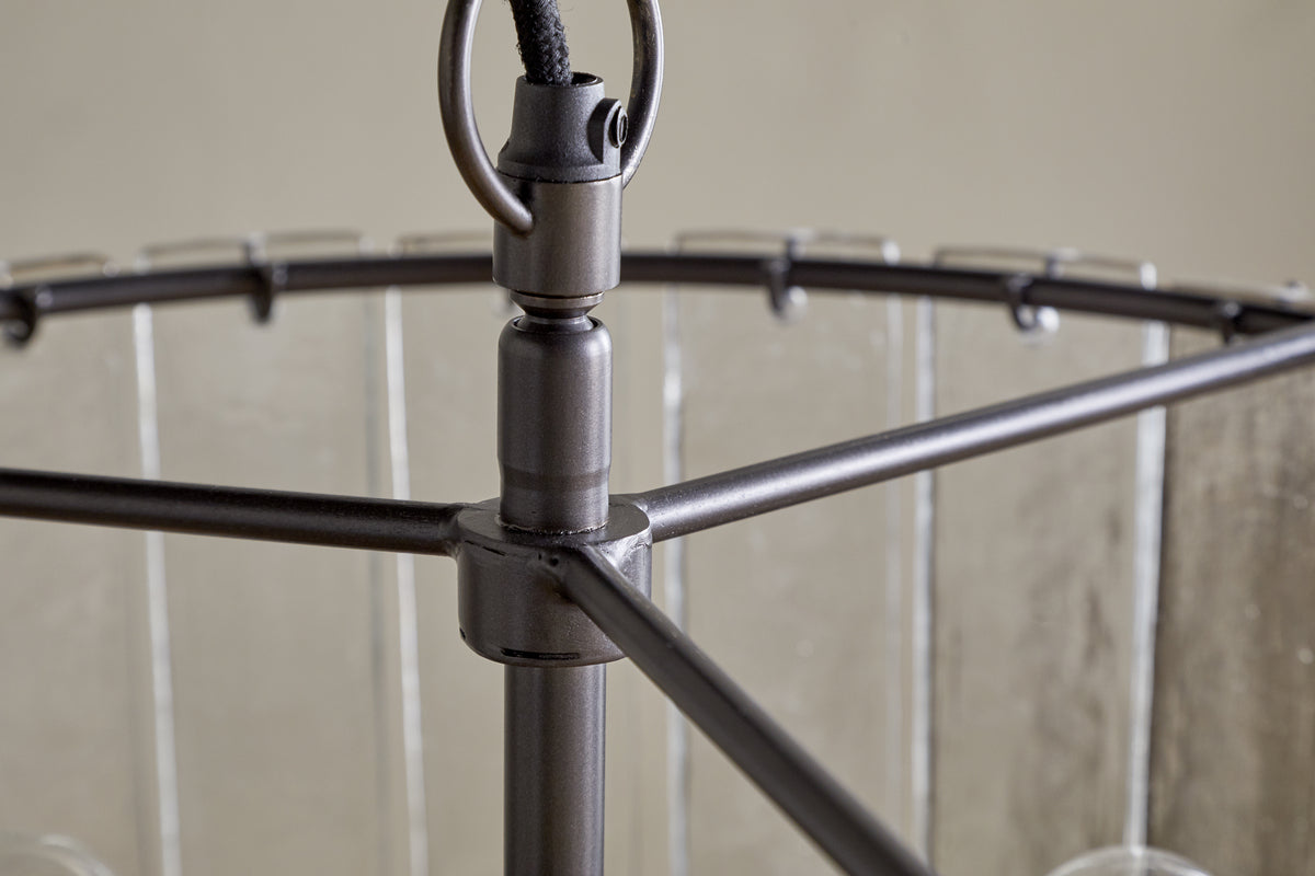 Close-up of the Nauka Statement Pendant by nkuku, featuring an aged bronze finish. The central rod links to three horizontal arms supporting a circular frame with clear glass panels, creating a refined, modern chandelier effect.