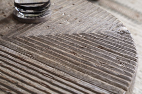 Close-up of nkuku’s Chakala Reclaimed Wood Coffee Table, featuring a chevron-patterned, textured surface with natural grooves and imperfections. A glass coaster or object is partially visible in the upper left corner.