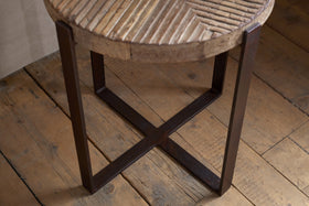 The nkuku Chakala Reclaimed Wood Side Table features a textured grooved seat that highlights natural wood grain and stands on four dark iron legs in an X shape, blending sustainable style with timeless design.