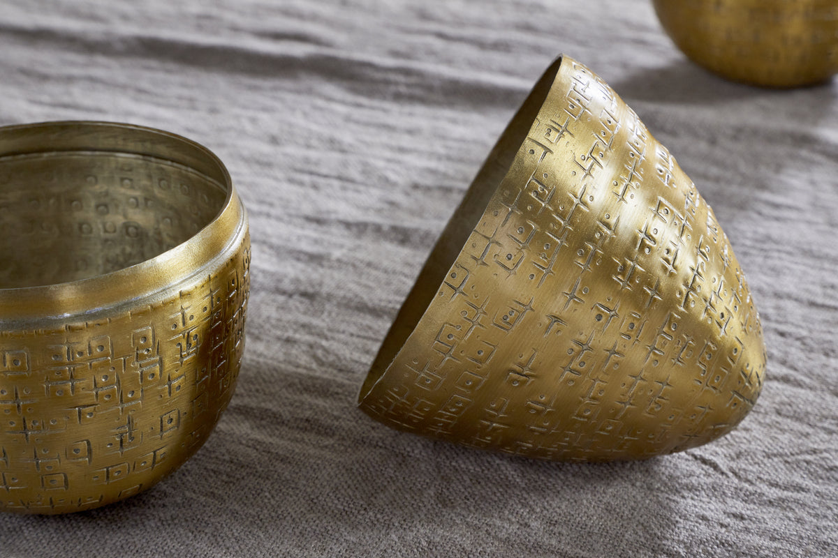 Two Mutti Hammered Opening Eggs by nkuku, crafted from antique brass, rest on textured beige fabric. One stands upright showing its intricate interior while the other lies open—each a beautiful keepsake with Easter egg–inspired charm.