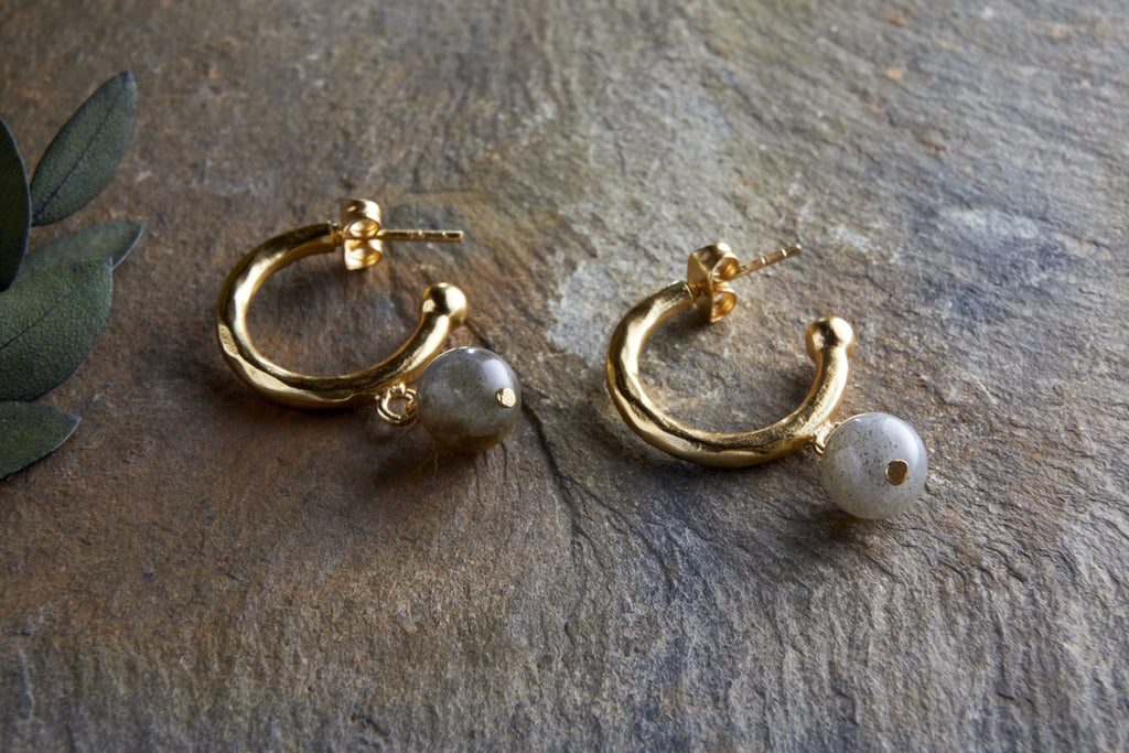 The Marai Labradorite Earrings by nkuku feature gold hoops with a hammered finish and elegant drop design, each adorned with a dangling round labradorite bead—a stylish jewellery gift.
