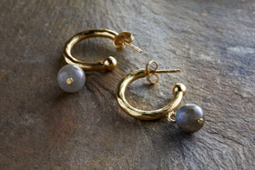 The Marai Labradorite Earrings by nkuku feature gold hoops with organic curves and a round, grayish labradorite bead drop, creating an elegant silhouette—an ideal jewelry gift.