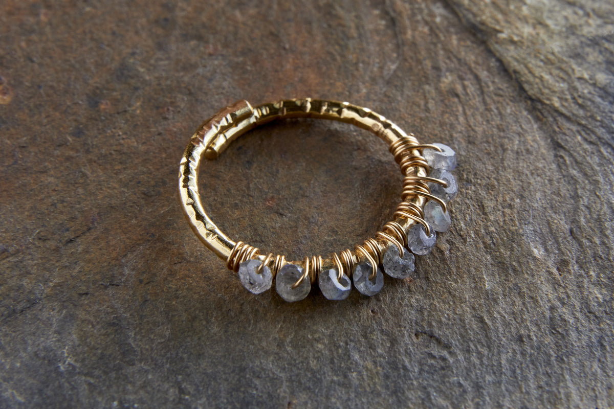 The nkuku Vani Labradorite Ring features a hammered gold-plated band with seven faceted labradorite stones wire-wrapped along one side, offering a rustic, handcrafted look with subtle sparkle.