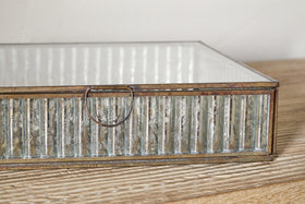 A close-up of the Malita Jewellery Box by nkuku, styled in antique brass with a mirrored base and mercury glass-inspired sides. It features a small circular handle and is set on light wood against a neutral background.