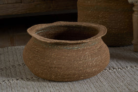 The nkuku Rana Short Basket - Natural & Moss features a handwoven round seagrass design with visible weave patterns and moss-green accents—ideal for natural home decor and pictured here on a textured, off-white rug.