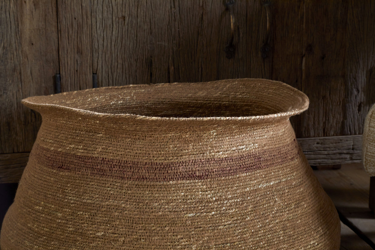 The nkuku Rana Wide Basket in Natural & Rust features a handmade, textured seagrass weave with subtle rust-toned bands and a gently flared rim, making it a stylish indoor storage solution against rustic décor.