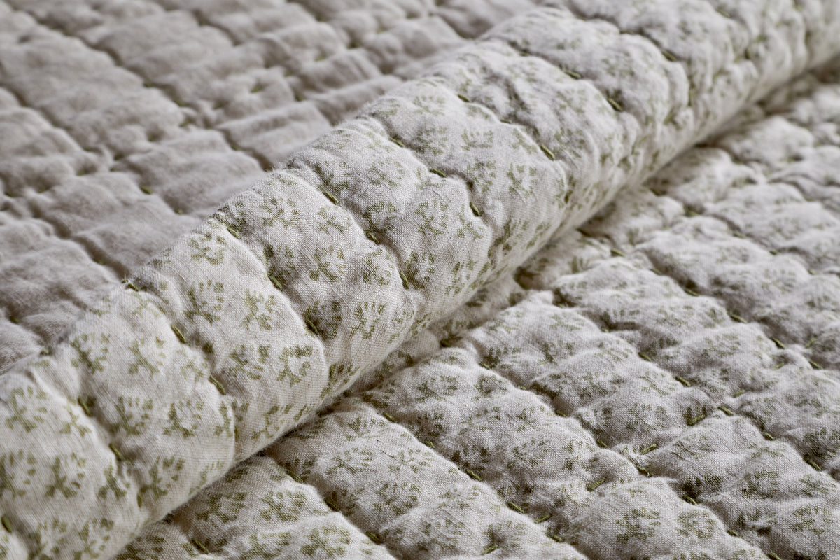 Close-up of the nkuku Peplu Cotton & Linen Screen Print Bed Quilt in sage green, featuring a soft, quilted grid pattern with floral motifs on an off-white background, inspired by Indian textile heritage.