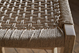 Close-up of the nkuku Aamani Mango Wood & Cord Counter Stool - Natural, featuring a thick, natural-colored rope seat woven in a crisscross pattern on a light mango wood frame. The detailed craftsmanship and texture are clearly visible. Wooden floor background.